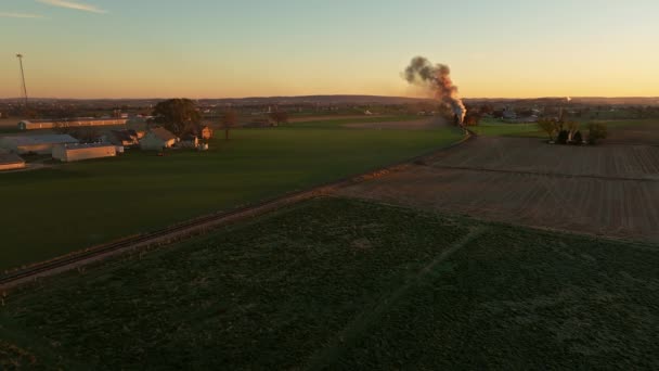 秋の朝に農地を通って旅行日の出に煙を吹いて接近する蒸気機関のドローンビュー — ストック動画
