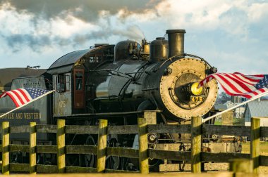 Ronks, Pennsylvania, December 3, 2022 - A View of a Classic Steam Passenger Train Approaching, With American Flags Attached to a Fence on a Sunny Summer Day