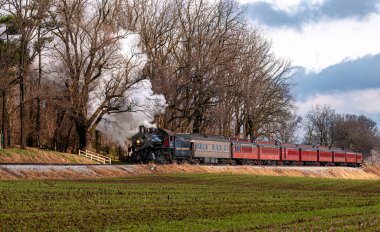 Ronks, Pennsylvania, December 3, 2022 - A View of a Classic Steam Passenger Train, Blowing Lots of Smoke and Steam, While Traveling in the Countryside on an Autumn Day