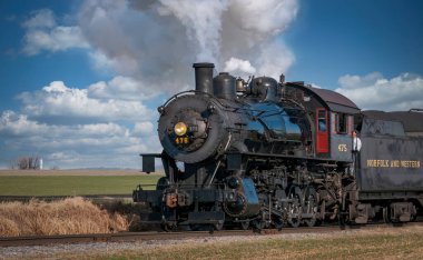 Ronks, Pennsylvania, December 28, 2022 - A View of a Classic Steam Passenger Train Approaching, Traveling Thru the Countryside, Blowing Smoke and Steam on a Winter Day