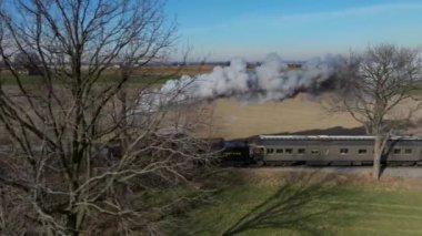 Ronks, Pennsylvania, December 28, 2022 - A Drone Parallel View of a Steam Passenger Train Traveling on a Single Track thru the Countryside, on a Winter's Sunny Day