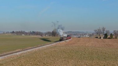 An Aerial View of a Steam Passenger Train Approaching Along a Single Train Track, Traveling Thru the Farmlands, on a Sunny Winter Day