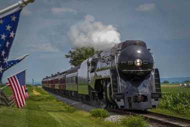 Güneşli bir yaz gününde Treni Gezen Thru Tarım Alanlarında Amerikan Bayrakları Çatışırken Bir Buharlı Yolcu Treni Yaklaşıyor