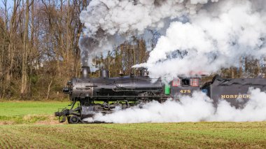 Ronks, Pennsylvania, December 4, 2022 - A View of a Classic Steam Passenger Train, Blowing Lots of Smoke and Steam, While Traveling in the Countryside on an Autumn Day