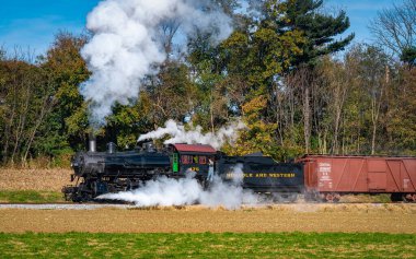 Ronks, Pennsylvania, November 8, 2021 - A View of a Restored Steam Freight Train Blowing Smoke and Steam Traveling Along a Rural Countryside on a Sunny Day