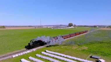 Ronks, Pennsylvania, November 8, 2022 - An Aerial Ahead and Parallel View of a Single Rail Road Track With a Steam Train Blowing Smoke on a Sunny Fall Day