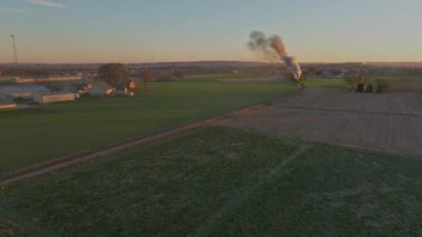 Gündoğumunda çiftliklerin havadan görünüşü, ahır ve çiftliklerle, Buharlı trenin yaklaşmasıyla Sonbahar sabahında bir sürü duman.