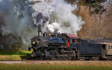 A View of a Classic Steam Passenger Train, Blowing Lots of Smoke and Steam, While Traveling in the Countryside on an Autumn Day