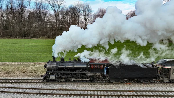 在冬季的日子里 一部蒸汽机车驶向旅行的特鲁田野和草原 吹来的白烟的侧角无人机视图 — 图库照片
