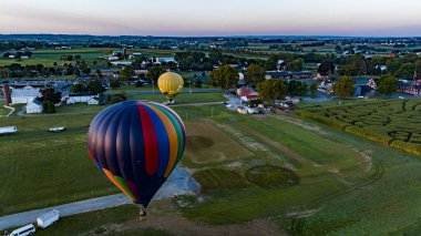 Güneşli bir yaz gününde, sabahın erken saatlerinde, Amerika 'nın kırsal kesimindeki bir tarladan iki sıcak hava balonu fırlatılışı üzerine bir hava görüntüsü.