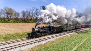 Antika Buharlı Yolcu Treni Thru Çiftlikleri 'ni geziyor, ekili ekinler, güneşli bir bahar gününde duman üflüyor.