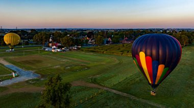 Kırsal Amerika 'da, güneşli bir yaz sabahı, Siyah Çizgili Sıcak Hava Balonunun Alçak Çayırlarda ve Çiftliklerde Yüzüşünün Hava Görüntüsü.