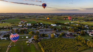 Pensilvanya 'nın kırsalında, güneşli bir yaz sabahında güneşin doğuşunda birden fazla sıcak hava balonu havada süzülüyor.