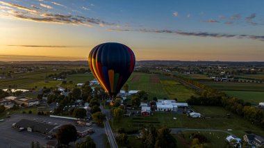 Güneşli bir yaz sabahı güneşin doğuşunda Pennsylvania kırsalında süzülen tek bir sıcak hava balonunun hava görüntüsü.