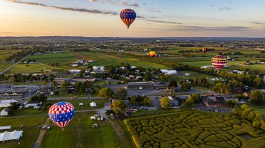 An Aerial View of Multiple Hot Air Balloons Floating Up Over Rural Pennsylvania During a Morning Launch on a Sunny Summer Day