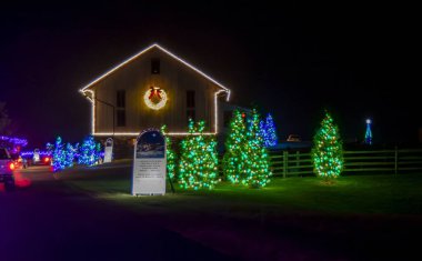 Beyaz Noel ışıkları ve yeşil ışıklarla çevrili bir çelenk ile özetlenmiş bir binanın gece manzarası, bir yazı ve noel gösterisiyle birlikte..