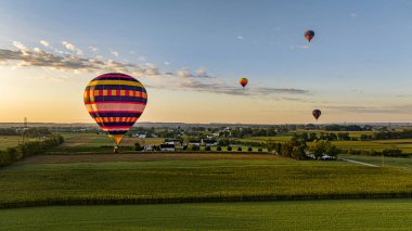 Canlı çizgili bir sıcak hava balonunun Zemine yakın süzülüşünün Havadan görünüşü Yumuşak bir ışığın altındaki yemyeşil tarlaların üzerinde.
