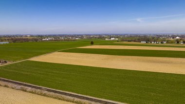 Geniş mavi gökyüzü altındaki küçük bir kasabanın sınırında belirgin yeşil ve bej desenli tarım alanları..