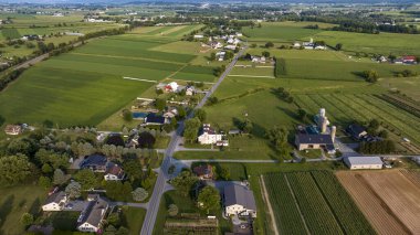 Çiftliklerle dolu yüksek açılı bir kırsal toplum manzarası, temiz sıralarda ekinler, arazide çaprazlama geçen yollar ve cadde boyunca yığılmış binalar..