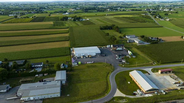 stock image Birds-Eye View Of Industrial Buildings Alongside A Railroad Track, Curved Roads, And Vast Agricultural Fields In A Rural Landscape At Dusk.