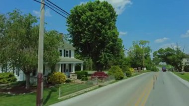 Bahar güneşinde güneşlenen evlerle dolu bir banliyö yolu boyunca sakin bir sürüş Amish atı ve at arabasının yanından geçerken.