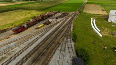 Eski tren vagonları ile dağılmış bir kırsal tren istasyonu, engin tarım alanları arasında yuvalar, sanayi ve çiftçiliğin yan yana gelişini gösteriyor..