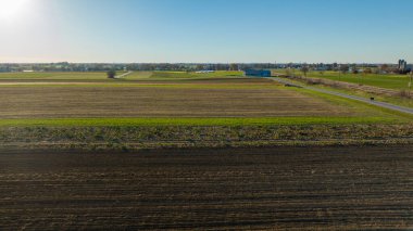 Açık mavi gökyüzünün altında, bu görüntü banliyö tarım arazilerini ve tarlaların ahenkli karışımını kapsıyor, emlak ve şehir planlama için ideal..