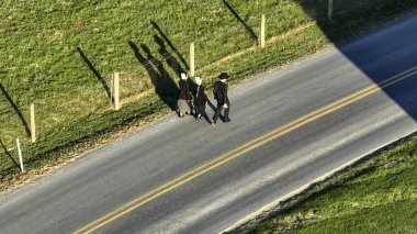 Ronks, Pensilvanya 14 Kasım 2023 - Güneşin batışı, üç kişinin uzun gölgeleri, kırsal bir yolda yürüyen Amish 'ler yoldaşlık ve topluluğun resmini çiziyor..
