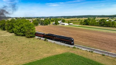 An evocative aerial view of a steam train puffing through picturesque rural farmlands, marked by vividly colored fields and pastoral settings. clipart