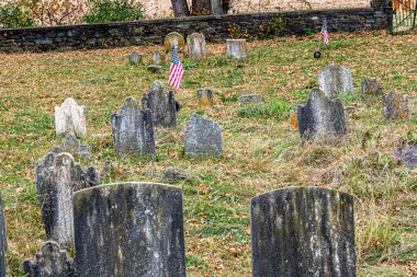 Eski bir mezarlığın dokunaklı görüntüsü yıpranmış mezar taşları ve düşmüş sonbahar yapraklarının arasına yerleştirilmiş Amerikan bayrakları, geçmişe saygılarını sunuyor..