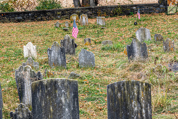 Poignant image of an old cemetery with weathered tombstones and American flags, nestled among fallen autumn leaves, showcasing a solemn tribute to the past.