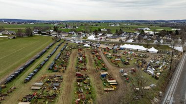 This Aerial image of an Amish Mud Sale, shows a comprehensive display of colorful farm machinery and equipment spread across a rural exhibition field with tents and visitors. clipart