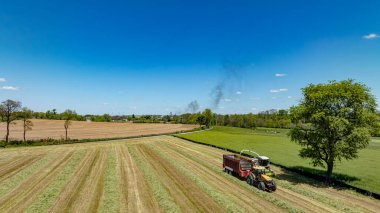 Geniş bir hava fotoğrafı, tarımın dinamik doğasını ön planda etkin hasat makineleri ile vurgular, karışık yeşillik ve kahverengi alanlar zeminine karşı kurulur.