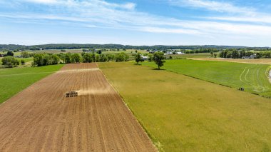 Önünde bir traktör, arkasında mavi bir gökyüzü olan bir alan. Alan çoğunlukla kahverengi ve yeşildir.