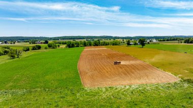 Önünde bir traktör, arkasında mavi bir gökyüzü olan bir alan. Alan çoğunlukla kahverengi ve yeşildir.