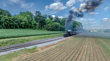 Ronks, Pensilvanya, ABD, 8 Haziran 2024 - Siyah Buharlı Lokomotif Kırmızı Yolcu Arabalarını Dolgun Yeşil Araziler ve Ormanlık Alanlarda, Açık Mavi Bulutlar Altında Çekiyor