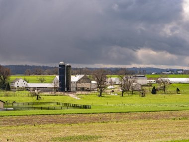 Ronks, Pennsylvania, ABD, 4 Nisan 2024 - Yeşil Alanlar ve Yuvarlanan Tepeler arasında Çıplak Bulutlu Gökyüzü Altında İki Uzun Silo ve Beyaz Binalı Resimli Bir Çiftlik