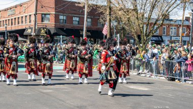 Lindenhurst, New York, ABD, 30 Mart 2024 - Geleneksel İskoç etek ve Bearskin Şapka Giyen Bir grup Gaydacı, Çevrelenmiş Seyirci Kalabalığıyla Renkli Bir Sokak Geçidi Gösterisinde