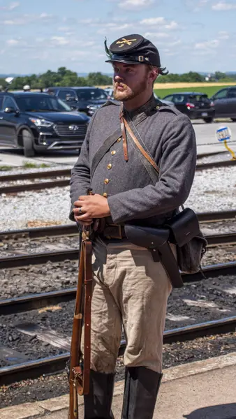 Strasburg, Pensilvanya, ABD, 8 Haziran 2024 - Gri Askeri Üniformalı ve Siyah Şapkalı Bir İç Savaş Canlandırıcısı Demiryolu Raylarında, Bir Tüfek Tutuyor ve Çağdaş İfade Ediyor