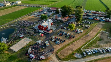 Ronks, Pennsylvania, ABD, 3 Temmuz 2024 - Kızıl ahır, yemek kamyonları, park alanı ve çeşmeli havuz manzaralı büyük bir toplantıya ev sahipliği yapan bir çiftlik görüntüsü.