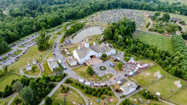 Elizabethtown, Pennsylvania, ABD, 4 Temmuz 2024 - Beyaz Ahırlı Geniş Kırsal Fuar Alanı, Küçük Kiliseler, Manzaralı Göl ve Yeşillikler Arasında Şenlik Yapan İnsanlar,