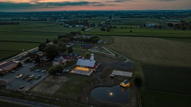 Ronks, Pennsylvania, ABD, 19 Temmuz 2024 - Alacakaranlıkta Sakin Çiftlik Sahnesi Beyaz Silolu Büyük Kırmızı Ahır, Aydınlanmış Taş Avlu, Yakın Bir Tuğla Evi, Genişletilmiş Yeşil Tarlalar ve