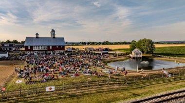 Ronks, Pennsylvania, ABD, 3 Temmuz 2024 - Kızıl Ahırın yakınında büyük bir kalabalık toplandı ve fıskiyeli küçük bir gölet güneşli bir günde açık hava etkinliğinin tadını çıkarıyor.