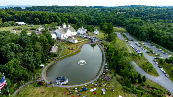 stock image Elizabethtown, Pennsylvania, USA, July 4, 2024 - Charming Rural Fairground With A Scenic Pond, White Barns, Small Churches, And People Enjoying Festivities Amidst Lush Greenery, Creating A Vibrant