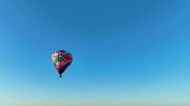 Kırmızı, beyaz ve mavi kareli renkli bir balon, açık havada özgürlük ve sükunet hissini vurgulayan, uçsuz bucaksız, berrak bir mavi gökyüzüne doğru süzülüyor.