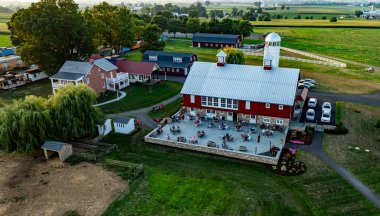 Ronks, Pennsylvania, ABD, 1 Ağustos 2024 - Misafirler akşam karanlığında yemyeşil tarlalarla çevrili kırsal bir çiftlik restoranının terasında yemeğin tadını çıkarıyorlar.