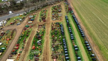 Yeşil ve kahverengi bir alanda çeşitli at arabaları ve renkli çiftçilik ekipmanlarının çoklu sıralı görüntüsü, çeşitli araçlarla kırsal tarım düzenini gösteriyor..