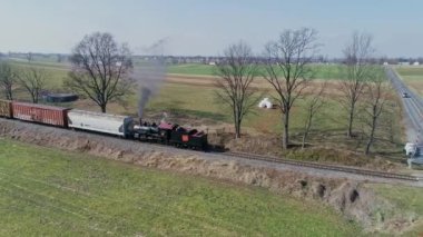 Ronks, Pennsylvania, ABD, 11 Mart 2022 - Güneşli bir günde, yemyeşil tarlalar boyunca ağaçların ve tarlaların yanından geçen bir buhar treni. Yüksek kalite 4k görüntü