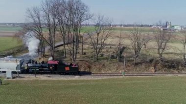 Ronks, Pennsylvania, ABD, 11 Mart 2022 - Eski model bir buhar treni, açık bir gökyüzünün altındaki yemyeşil alanlardan geçerek raylar boyunca tıkırdıyor. Yüksek kalite 4k görüntü