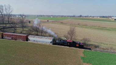 Ronks, Pennsylvania, ABD, 11 Mart 2022 - Eski model bir buhar treni, açık bir gökyüzünün altındaki yemyeşil alanlardan geçerek raylar boyunca tıkırdıyor. Yüksek kalite 4k görüntü